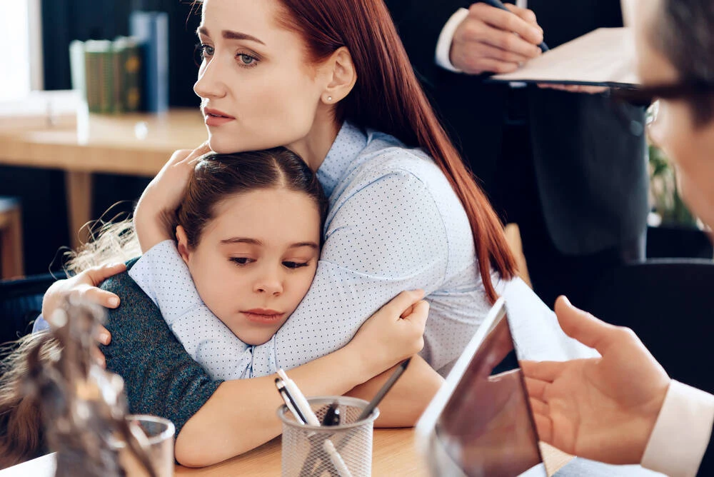 Red-haired sad woman hugs little upset girl sitting in lawyer's office for divorce.